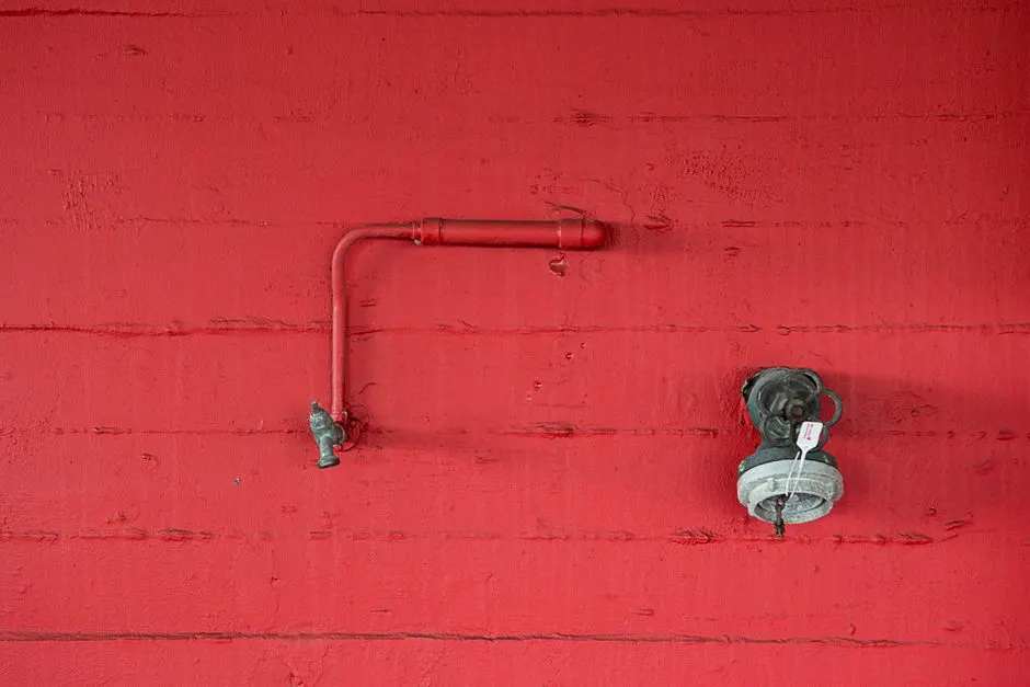 Close-up of a red wall featuring an industrial faucet and pipeline. Minimalist design.